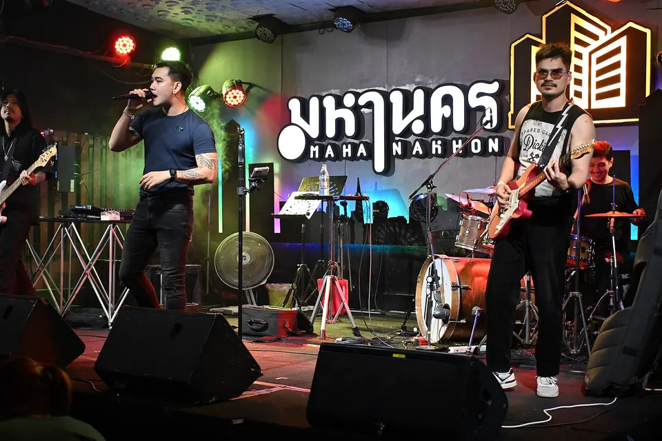Photo: a singer and two guitarists on the Mahanakhon stage, its name in neon behind them