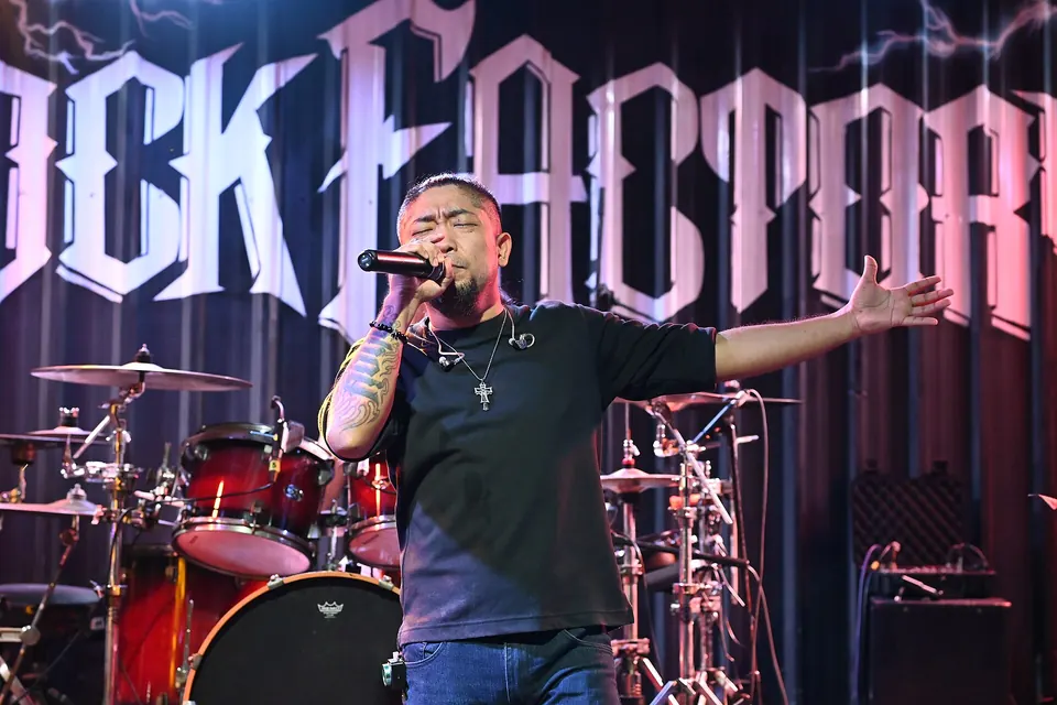 Photo: a singer with arms wide on the stage at Rock Factory, its name in big letters behind the drum kit