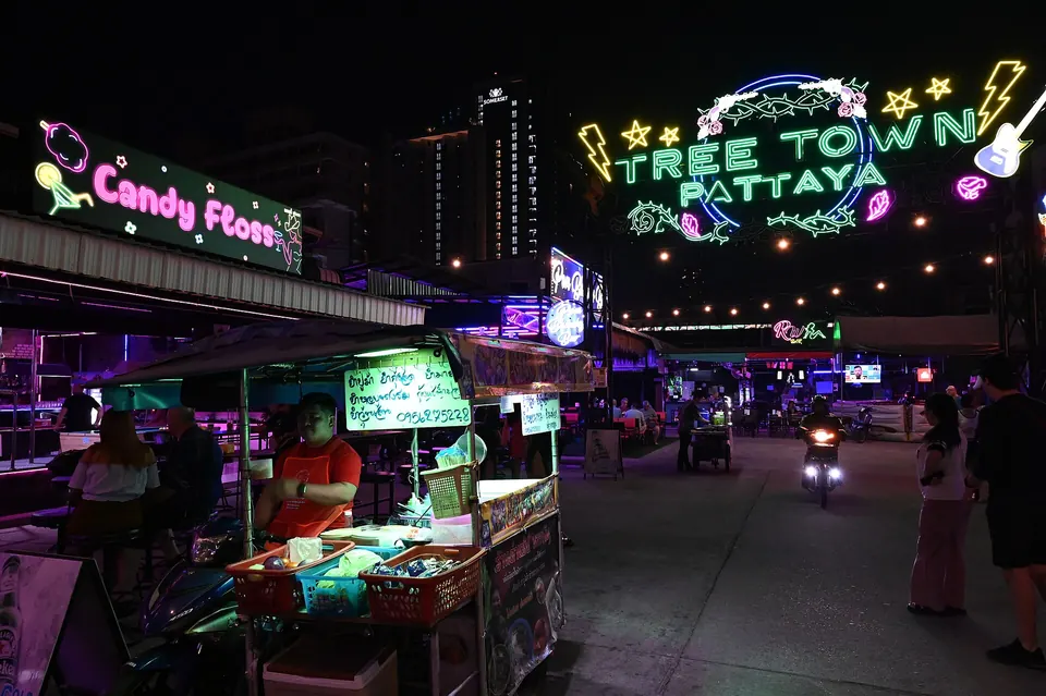 Photo: the Tree Town Pattaya sign in green neon over food stalls and an open lane at night